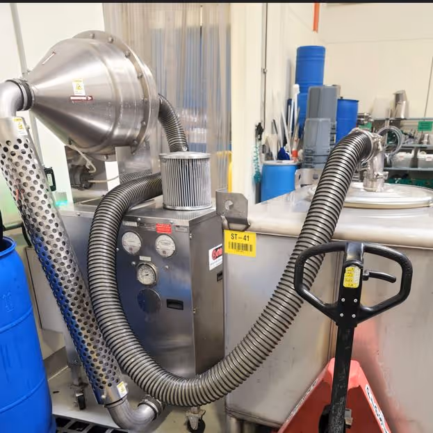 Sistema de transferencia por vacío en acero inoxidable fabricado a la medida en una planta de proceso industrial, con un tanque de almacenamiento inclinado identificado como "ST-41", mangueras flexibles negras, manómetros en un tablero central y una toma de aire con protector perforado.