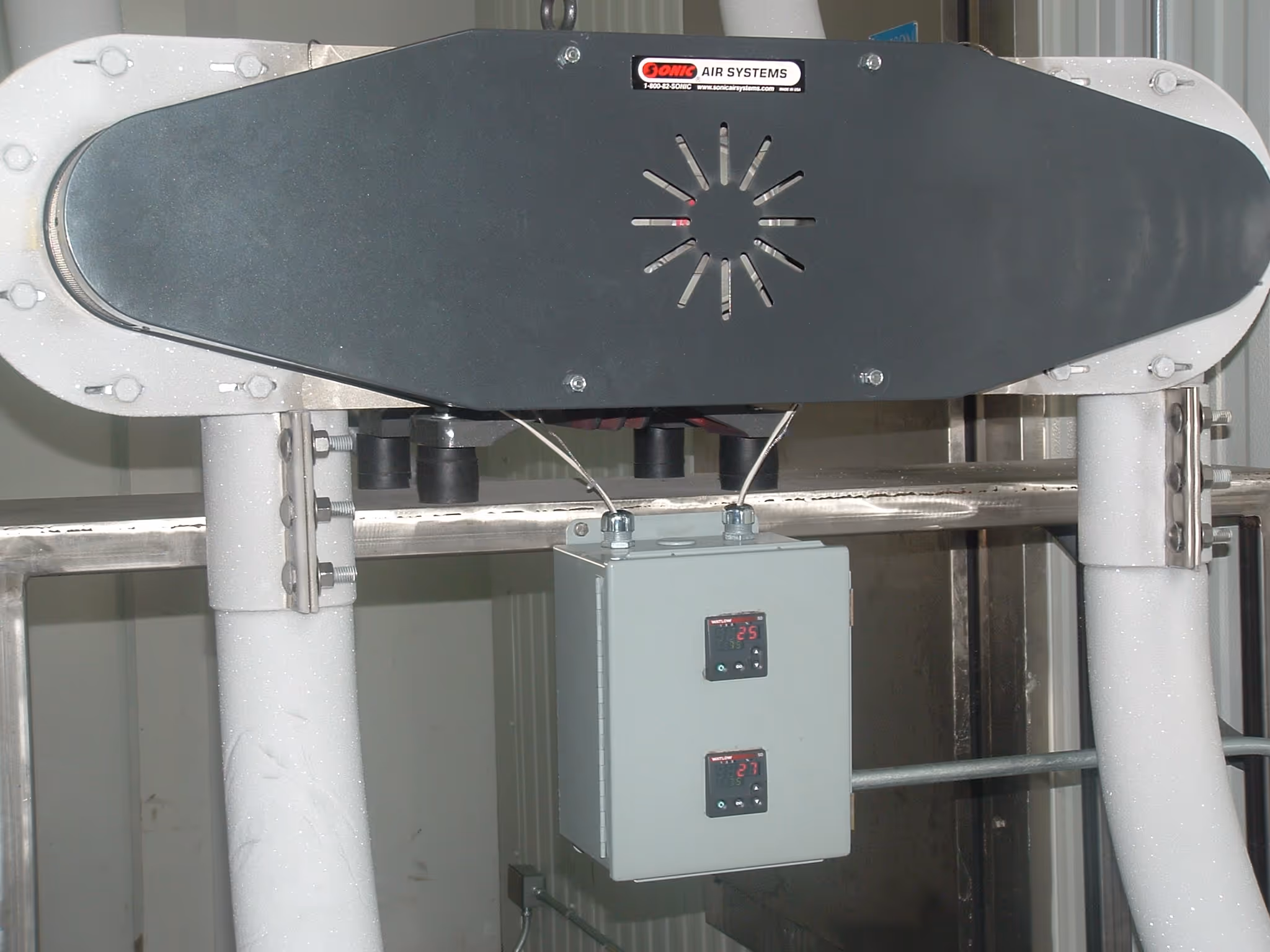 Unidad industrial de calentamiento de aire de Sonic Air Systems con dos entradas de tubería grises y un tablero de control digital con dos lecturas.